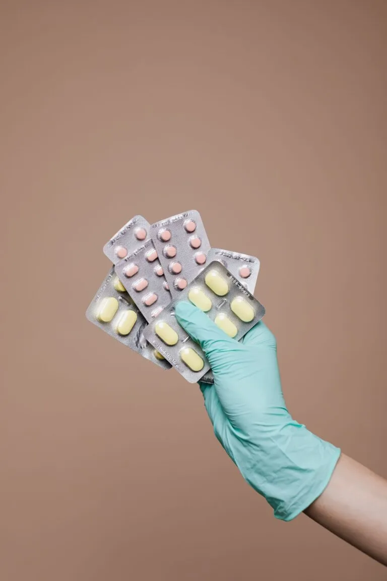 Mână cu mănușă ținând blistere cu medicamente pentru predare responsabilă