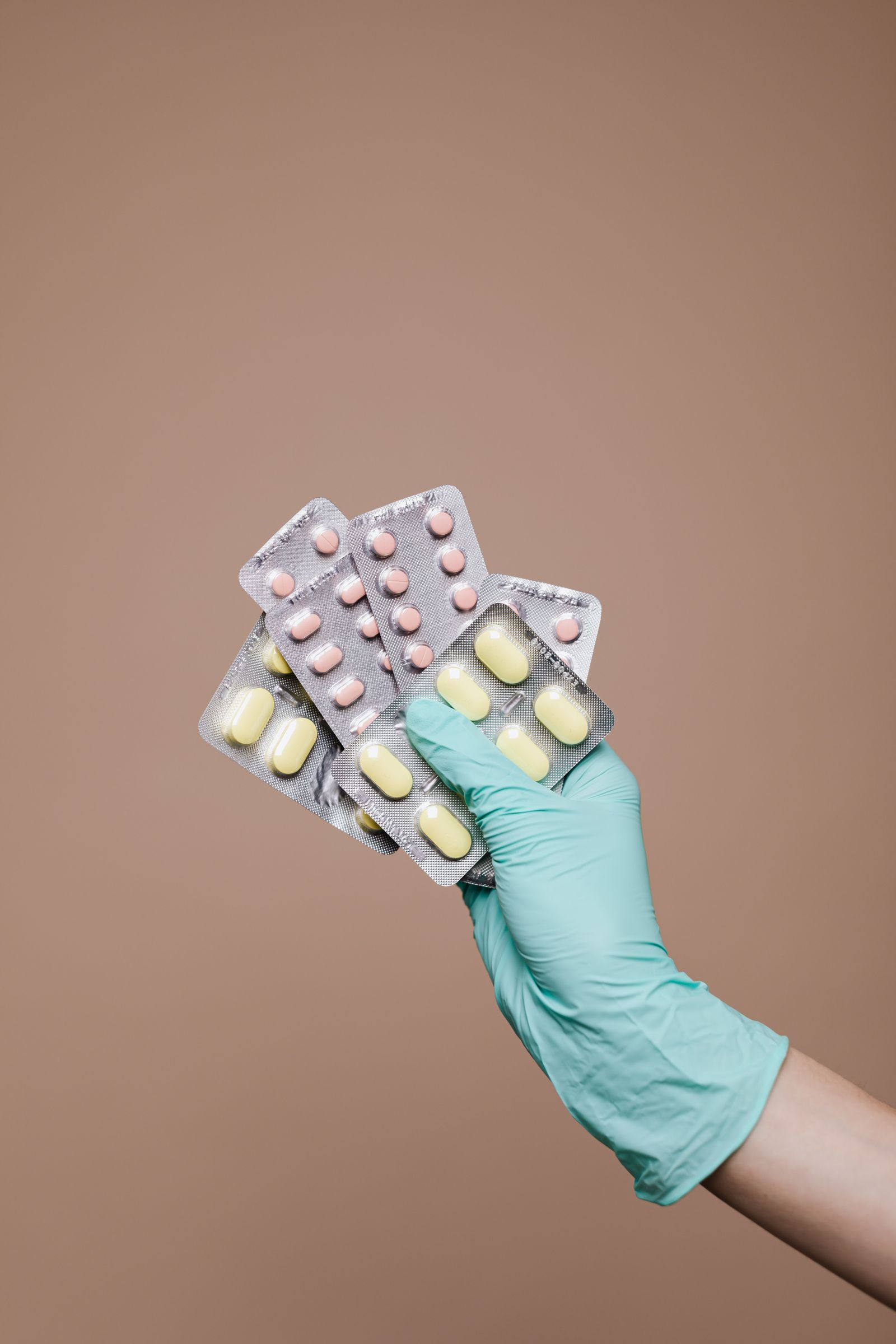 Mână cu mănușă ținând blistere cu medicamente pentru predare responsabilă